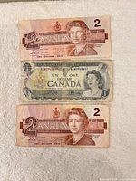 Fronts of two 1986 $2 notes and one 1954 $1 note laid on white towel