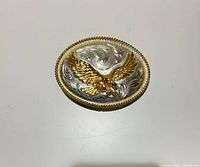 Front view of oval buckle showing silver scroll engraving and gold-tone eagle