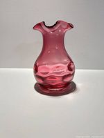 Profile view of cranberry glass vase showing coin-dot pattern and ruffled rim
