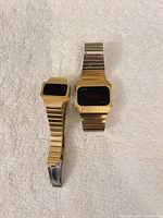 Two gold-tone Timex red LED digital watches displayed on towel
