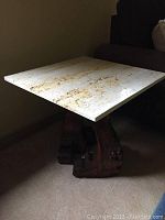 Side view of the square marble table showing the marble top and carved wooden piano legs base