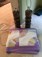 Photo showing two solid wood lamps with carved patterns and a folded vintage fan pattern quilt on the floor
