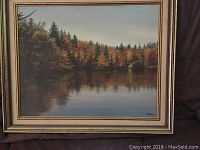 Full front view of the oil on canvas painting showing a lake surrounded by trees with autumn colors, and its surrounding framed border.