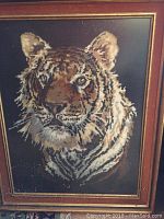 Close-up photo of the needlepointed tiger artwork showing detailed stitching and colors on dark fabric.