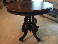 Front angled view of an antique solid wood round side table on casters showing carved legs and top surface.
