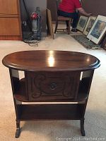 Front view of the small oval solid wood side table showing the carved door front and brass capped feet.
