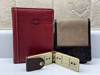 Three items: red passport holder, tan/black card wallet, folded cribbage board open