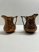 Front view of both copper lustreware jugs showing deer scenes and overall form