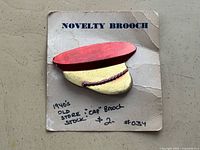 Brooch on original card showing cap design and text