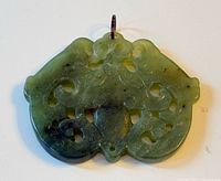 Front view of carved green jade pendant showing openwork details and bail