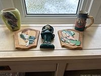 Front view of all items: three chalkware plaques, Art Deco fish vase, sailor character jug