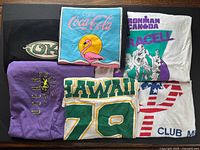 Six folded graphic T-shirts showing all designs