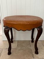 Front view of oval leather bench showing cabriole legs and ram’s feet