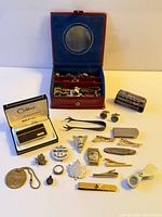 Overview of entire lot with red accessory case, boxed Colibri lighter, pocket knife, whistle, clips, pins and other items