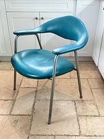 Front angled view showing turquoise leather seat, curved back, tubular steel legs and arms