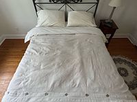 Full view of queen bed made up with white embroidered duvet cover, sheets and pillowcases