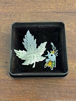 Both jewelry pieces in presentation box: maple leaf brooch and rooster pendant