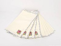 Fan arrangement of all ten cream napkins showing embroidered corners