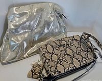Front view of both purses, JuJuBe snakeskin bag in front, silver satchel behind