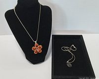 Both necklaces displayed: flower pendant on bust, round pendant in tray