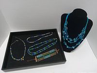 Overview of five jewelry pieces displayed on tray and bust