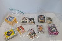 Multiple stacks of assorted baseball cards in plastic bags on tabletop
