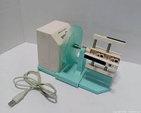 Front view of turquoise Spin It PRO tumbler turner with USB cable visible