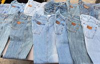 Ten pairs of Wrangler jeans laid flat showing light blue washes and back pocket leather patches