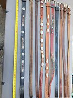 11 leather belts laid out showing full length with measuring tape