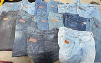 All 12 Wrangler jeans spread out showing variety of washes and logo patches