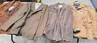 All four jackets laid out on table left-to-right brown suede, olive cotton, grey suede, tan suede