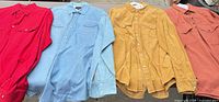 Four shirts laid out side by side: red, light blue denim, mustard corduroy, rust orange