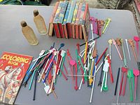 Group view of swizzle sticks, books stack, coloring book and two glass bottles on table