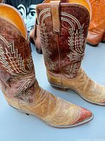 Side view of both boots showing two-tone leather, stitched toe caps, embroidered shafts, and overall wear