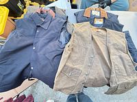 Overhead view showing navy vest left, tan vest right, additional jackets underneath