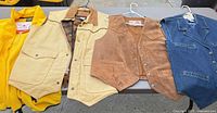 Four vests laid out on table: yellow fleece, tan canvas, brown suede, blue denim