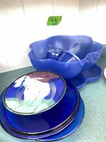 Overall view of blue glass plates stacked with plastic scalloped serving pieces beside
