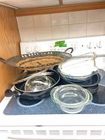Overall view of stacked glass bowls, metal pans, lids and decorative tray on stovetop