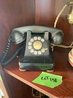 Front view of black rotary dial telephone on shelf