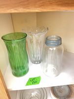 All three vessels on shelf: green vase, clear vase, clear jar with lid