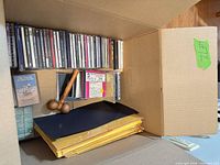 Row of CDs, cassette tape, CD rack base, stack of padded mailers visible inside box