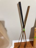 Full view of two wooden shaft golf clubs leaning against wall