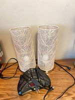 Pair of cylindrical table lamps with white swirl fabric shades, bulbs visible, cords and alarm clock radio on wooden surface