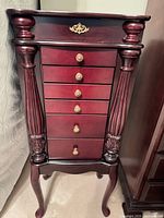 Front view of dark cherry standing jewelry cabinet showing six drawers, fluted columns, cabriole legs