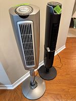 Silver Lasko and black Senville tower fans standing side by side