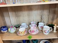 Full shelf showing all teacups, mugs, decanter, green dish, blue pot, trinket pot, angel figurine