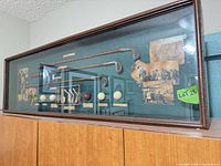 front view of wall display case showing clubs, balls, plaque, prints
