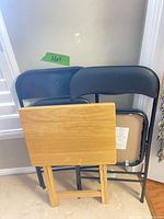 Two black metal folding chairs and folded wooden TV tray