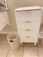 Front view of white resin cupboard with gold pulls and matching waste bin