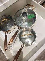 Three stainless steel Cuisinart pots with copper handles and two glass lids in drawer